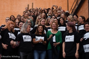 Massor av kvinnor i en trappa, alla med svarta tröjor med vid ruta på bröstet. I rutan en # och handskriven text