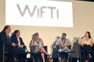 Five people sitting in chairs on a stage talking, the text Wift in the background